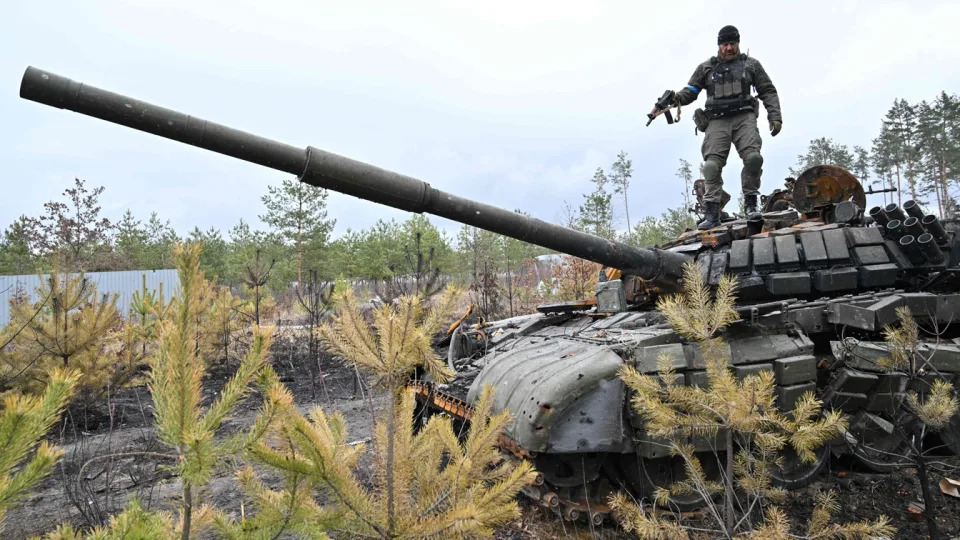 A Ukrainian serviceman stands on the turret of a destroyed Russian army tank.