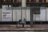 A man sits at a bus stop as wooden panels barricade shops because of on-going protests on Saturday, June 5, 2021 in downtown Portland, Ore. City officials insist Portland is resilient as they launch a revitalization plan — in the form of citywide cleanups of protest damage, aggressive encampment removals, increased homeless services and police reform — to repair its reputation. (AP Photo/Paula Bronstein)