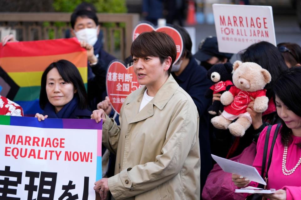 One of the plaintiffs, in a beige coat, center, speaks in front of media members by the main entrance of the Tokyo district court (AP)