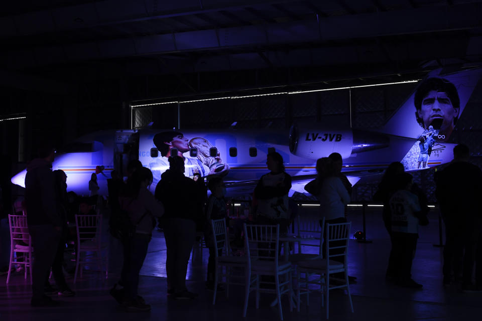 Un grupo de fanáticos se reúnen durante la presentación de una aeronave dedicada al fallecido futbolista, en una base militar en Morón, en las afueras de Buenos Aires, Argentina, el sábado 23 de julio de 2022. El avión partirá después en una gira por el mundo, que visitará Brasil, Colombia, México y Estados Unidos antes de llegar a Europa y hacer parada en Roma y Nápoles _dos lugares míticos en la carrera del 10_ y aterrizar en el Mundial de Catar. (AP Foto/Gustavo Garello)