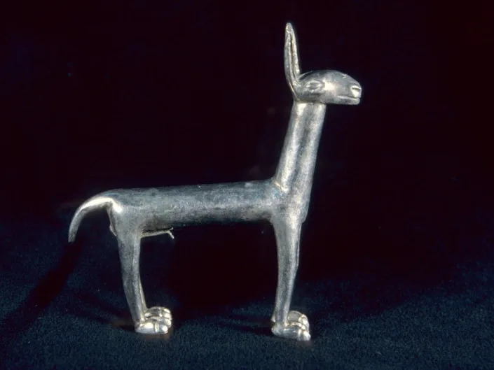 A statue made of silver as a likeness of a Llama is shown on a dark background.
