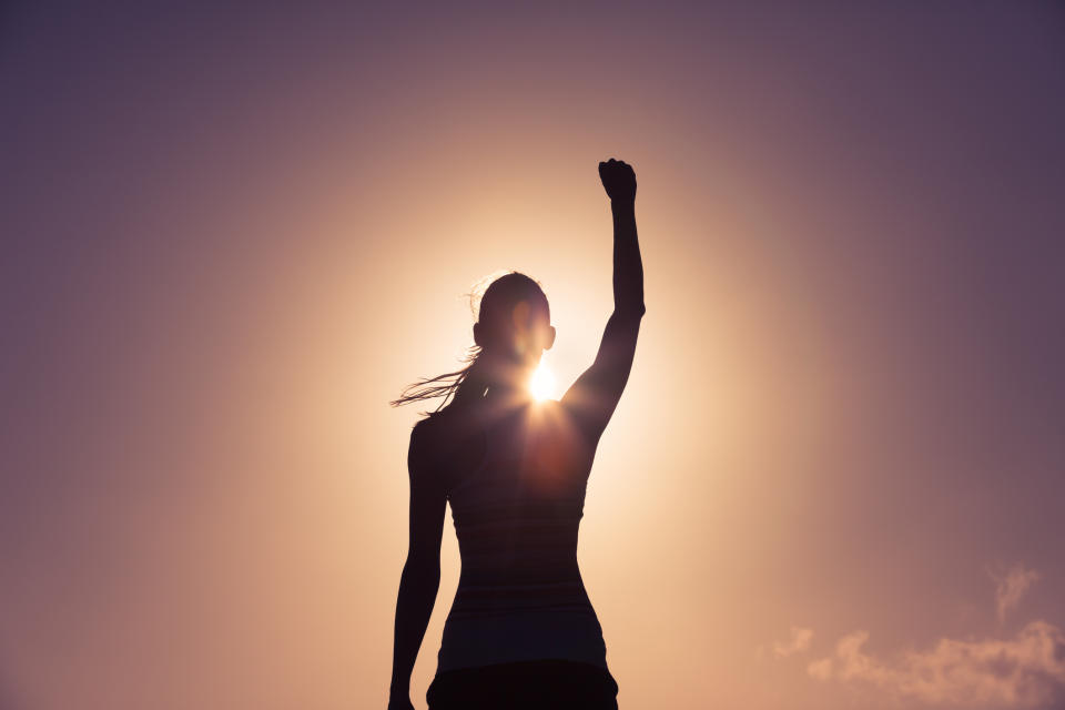 Silhouette of a woman raising her fist to the sky.