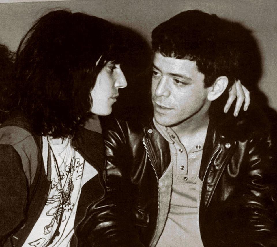 patti smith wraps an arm around lou reed's shoulders as he looks toward her speaking