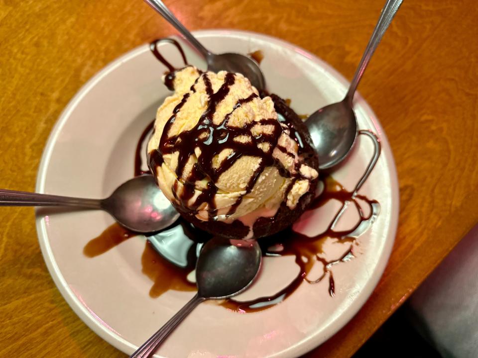 Brownie at Texas Roadhouse topped with vanilla ice cream and chocolate syrup in a bowl with four spoons