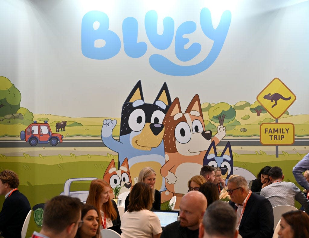 People sitting in front of a mural of Bluey and her sister.