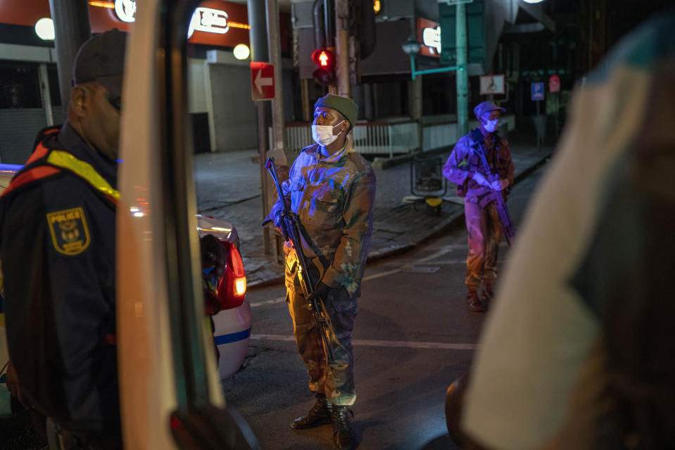 South African Defense Forces and police check a minibus driver who violated the lockdown downtown Johannesburg, South Africa, Friday, March 27, 2020. Police and army started patrolling moments after South Africa went into a nationwide lockdown for 21 days in an effort to mitigate the spread to the coronavirus. The new coronavirus causes mild or moderate symptoms for most people, but for some, especially older adults and people with existing health problems, it can cause more severe illness or death.(AP Photo/Jerome Delay)