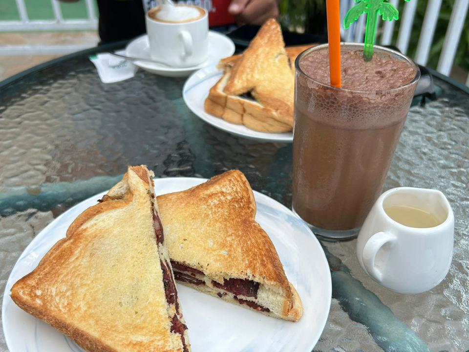 A sandwich with sausage and a cup of iced Timorese coffee