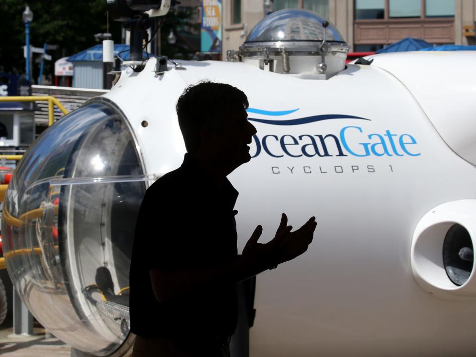 silhouette of man gesturing in front of white submersible with words oceangate on the side