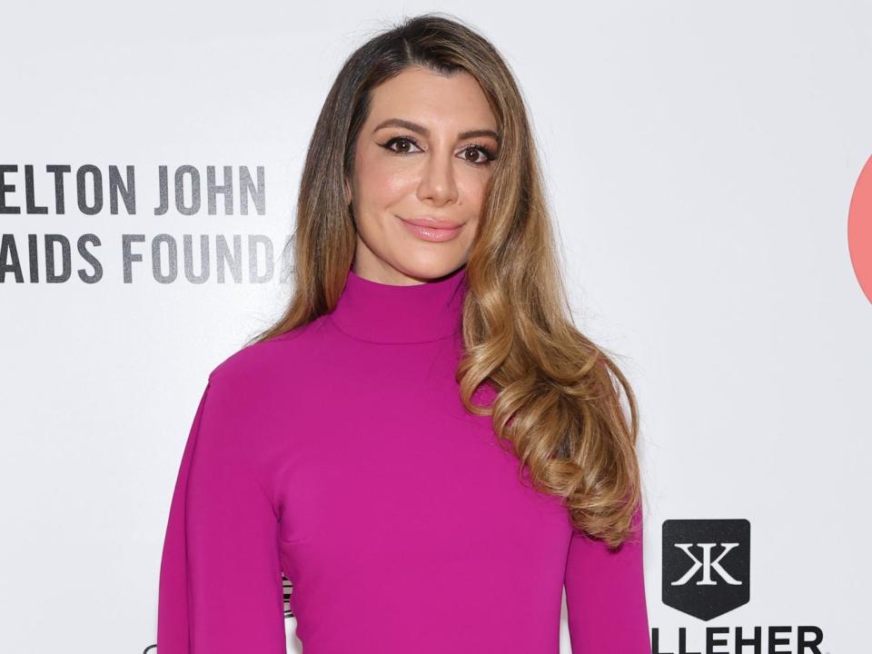 Nasim Pedrad with curled hair down one shoulder and magenta dress with white background