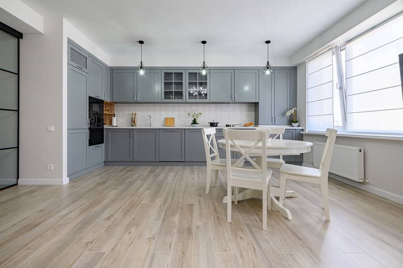 Trendy grey and white modern kitchen with white round dining table in studio apartment