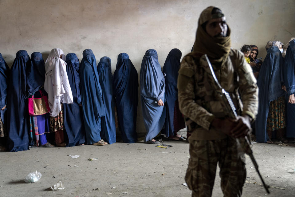 A Taliban fighter stands guard as women wait to receive food rations distributed by a humanitarian aid group, in Kabul, Afghanistan, Tuesday, May 23, 2023. (AP Photo/Ebrahim Noroozi)