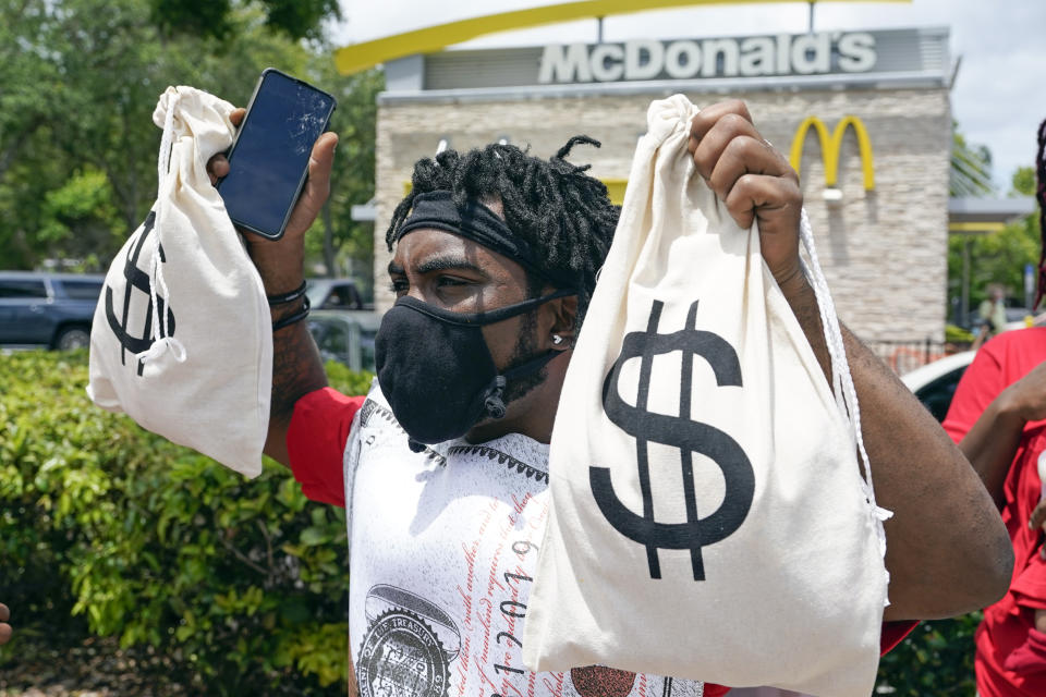 A McDonald's worker holds up bags to bring attention to the companies profits as he takes part in a 15-city walkout to demand $15hr wages Wednesday, May 19, 2021, in Sanford, Fla. (AP Photo/John Raoux)