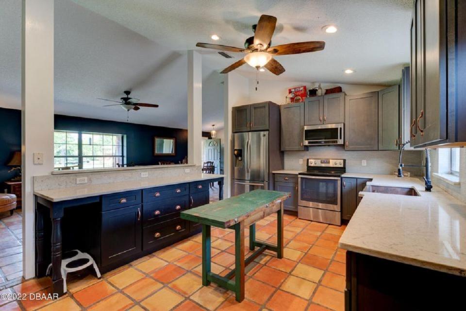 The artistically updated kitchen features a copper farmhouse sink, gorgeous grey and navy-blue cabinets with copper hardware, solid-wood cabinets and luxurious granite countertops.