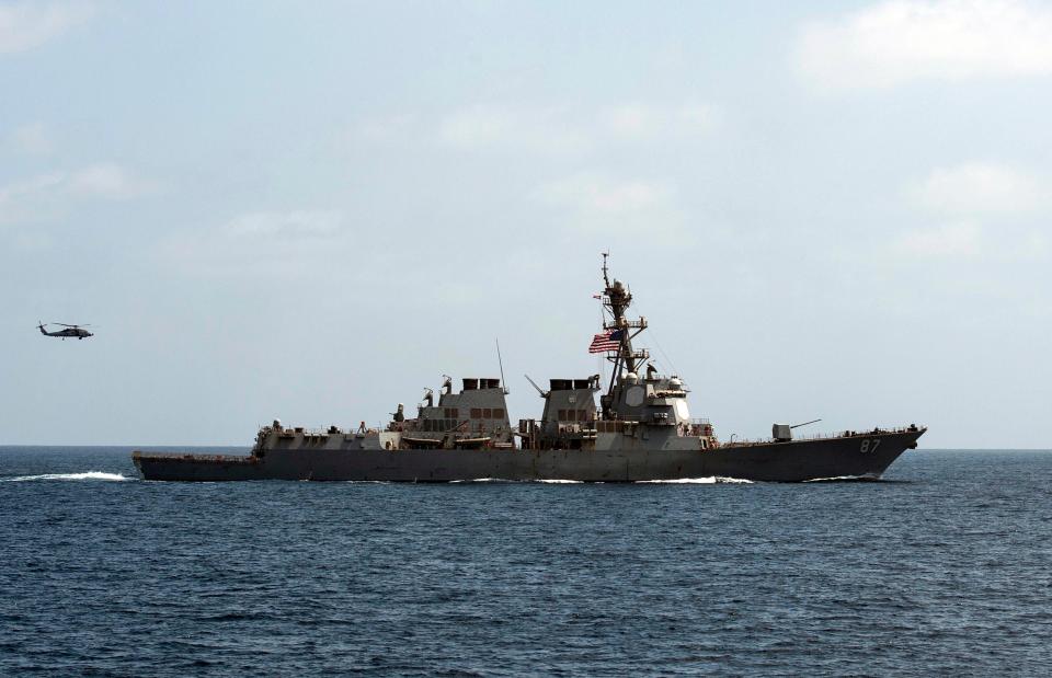 Destroyer USS Mason sails the open ocean with a helicopter trailing behind.