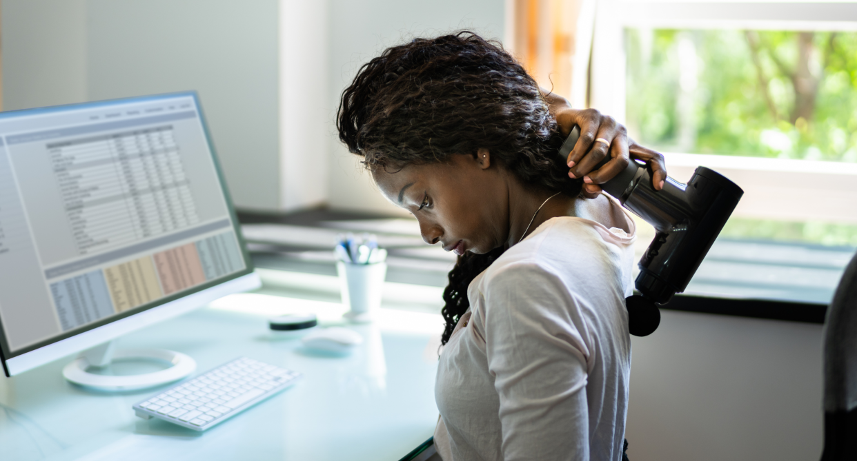 woman sitting at desk holding massage gun on back shoulder