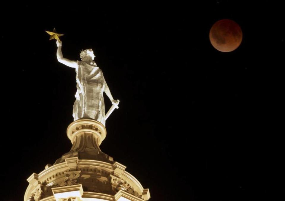 The moon glows a red hue over the Goddess of Liberty statue atop the Capitol in Austin during a total lunar eclipse April 15, 2014.