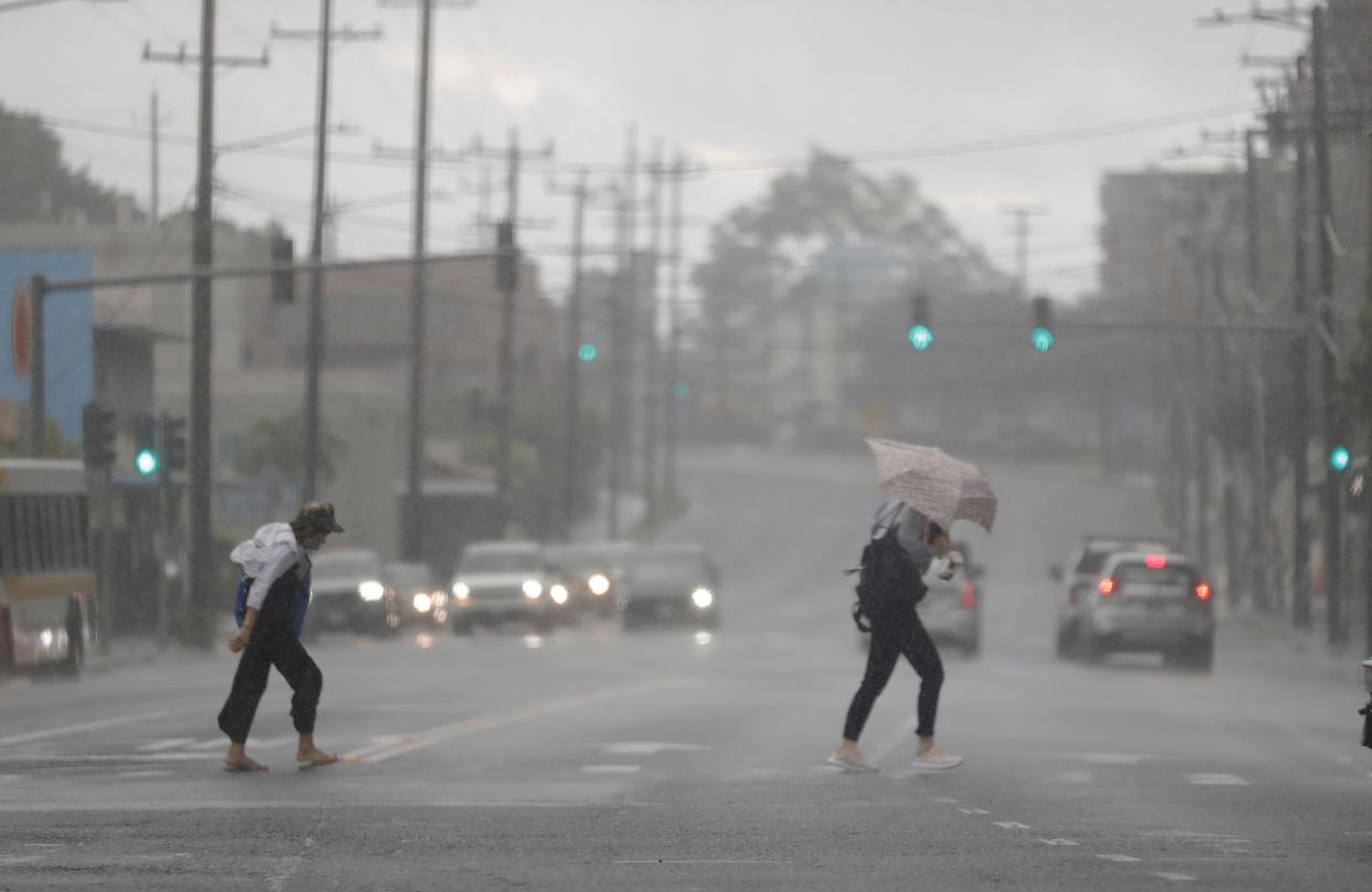 Two pedestrians make their way through a downpour across South King Street on Monday, Dec. 19, 2022, in Honolulu. (Jamm Aquino/Honolulu Star-Advertiser via AP)