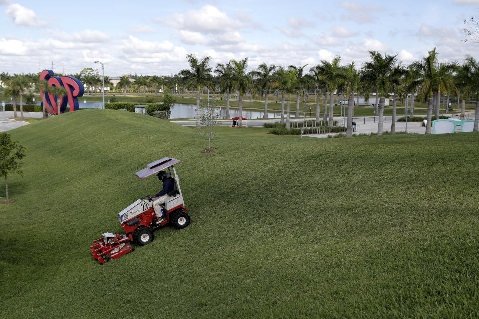 A worker mows the berm outside the Washington Nationals spring training baseball facility, Monday, March 16, 2020, in West Palm Beach, Fla. (AP Photo/Julio Cortez)