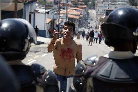 A boy with blood on his chest and hand gestures in front of police after 14-year-old student Kluiver Roa died during a protest in San Cristobal February 24, 2015. REUTERS/Carlos Eduardo Ramirez