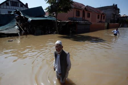 Kashmiri men pass a damaged house as they wade through a flooded street in Srinagar September 14, 2014. REUTERS/Danish Ismail