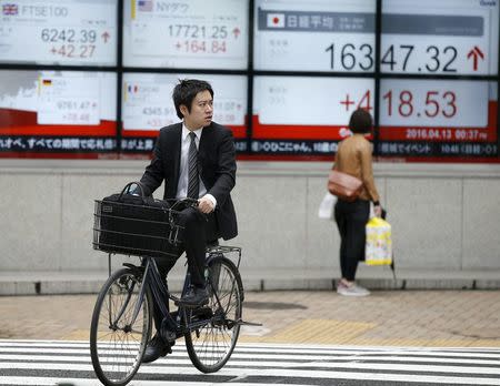 A man cycles in front of an electronic board showing Japan's Nikkei average (R) outside a brokerage in Tokyo, Japan, April 13, 2016. REUTERS/Toru Hanai