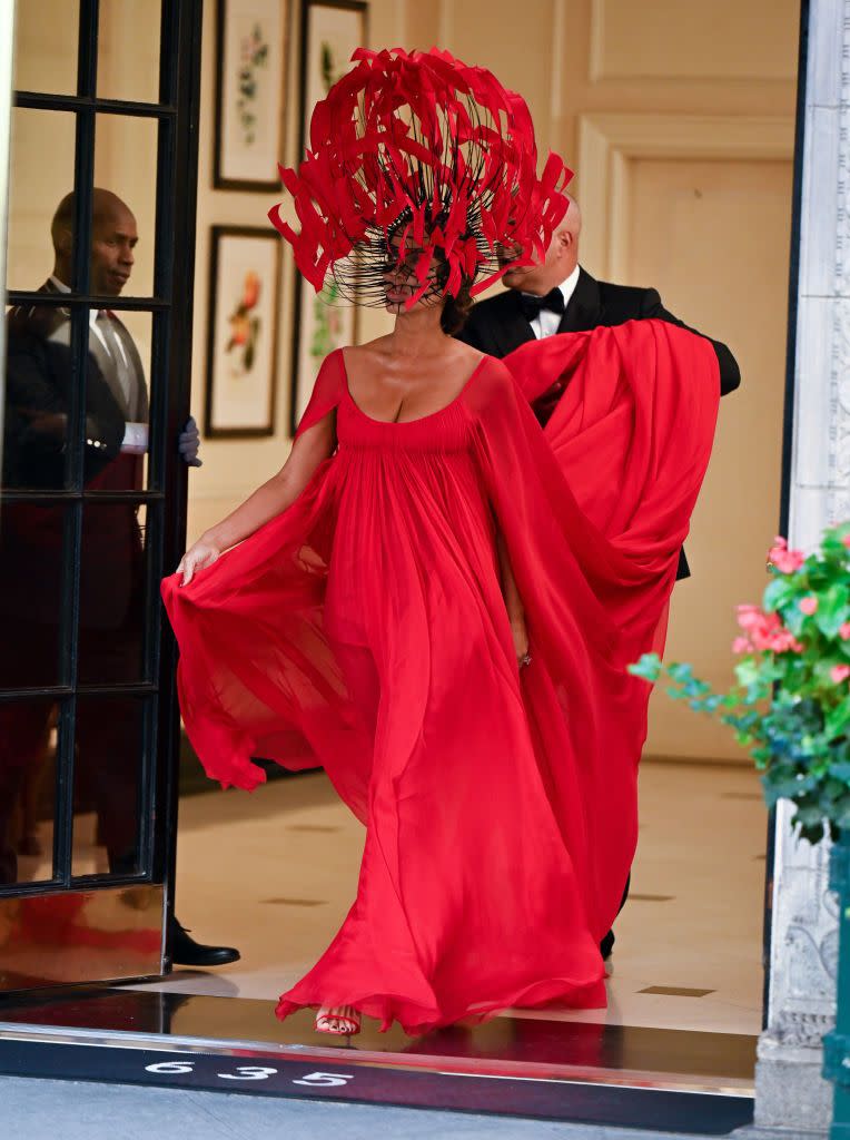 <p>In a red monochrome look featuring a larger-than-life headpiece with a flowing red gown and train. </p>