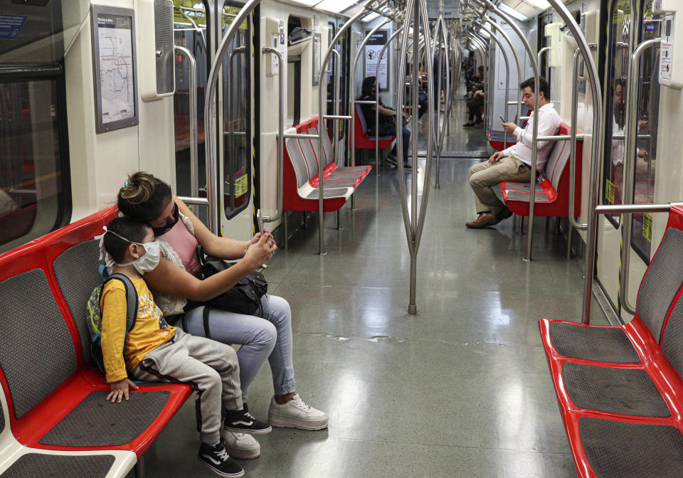 Una mujer y un niño con mascarillas como precaución contra un nuevo coronavirus se toman un selfie dentro de un metro casi vacío en Santiago, Chile, el viernes 20 de marzo de 2020. (Foto AP/Esteban Félix)