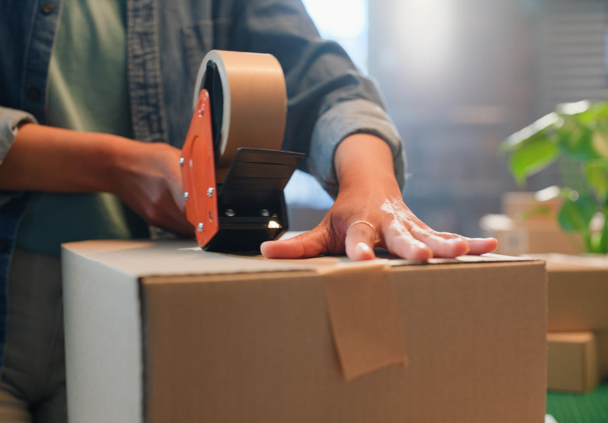 A close-up view of someone using their hands to tape a box using a tape dispenser.