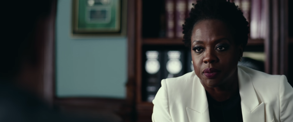 A screenshot from Widows, of Viola Davis wearing a white suit, sitting in an office looking mad