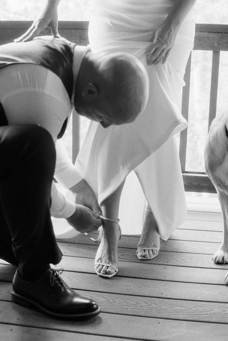 A man helps a bride put her shoes on in black and white.