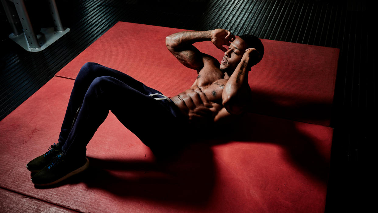  Shirtless man performing abdominal crunch exercise on floor. 