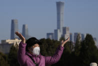 A woman wearing a mask makes a gesture for a photo near the city skyline seen from the Temple of Heaven Park in Beijing, Thursday, Dec. 8, 2022. In a move that caught many by surprise, China announced a potentially major easing of its rigid "zero-COVID" restrictions, without formally abandoning the policy altogether. (AP Photo/Ng Han Guan)