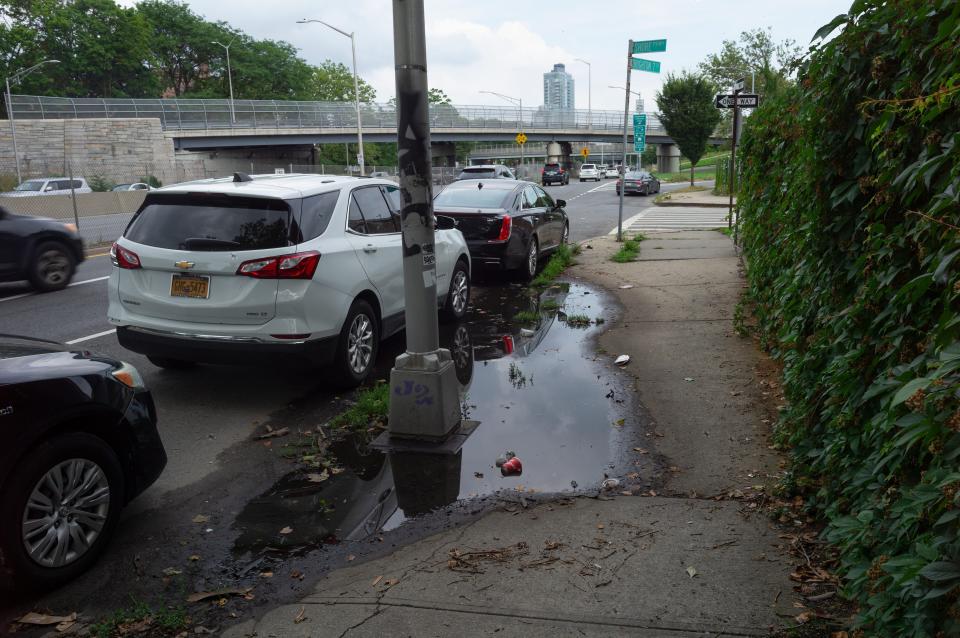 Puddles and cars are seen along a side road near a freeway.