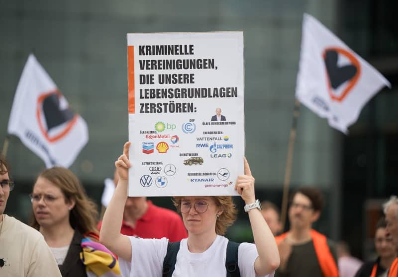A protester holds a sign "Criminal organizations that destroy our livelihoods:" at a demonstration on the occasion of the indictment of the Neuruppin prosecutor against five members of the Last Generation on charges of "forming a criminal organization".  Sebastian Christoph Gollnow/dpa