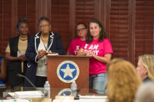 Four women stand behind a lectern, listening.