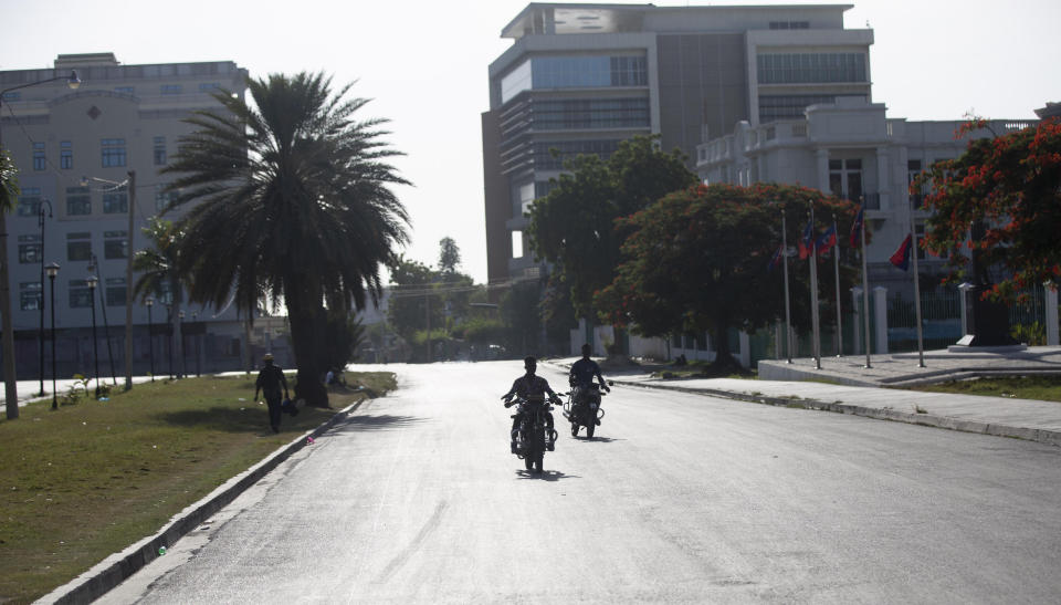 People ride their motorcycles on a street empty of traffic near the National Palace in Port-au-Prince, Haiti, Wednesday, July 7, 2021. Gunmen assassinated Haitian President Jovenel Moise and wounded his wife in their home early Wednesday. (AP Photo/Joseph Odelyn)