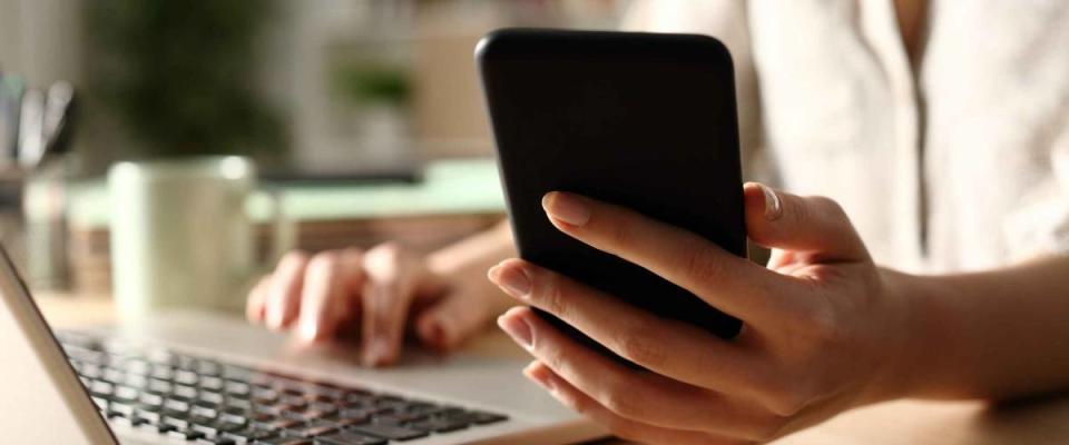 Close up of woman hands using laptop checking smart phone at night at home