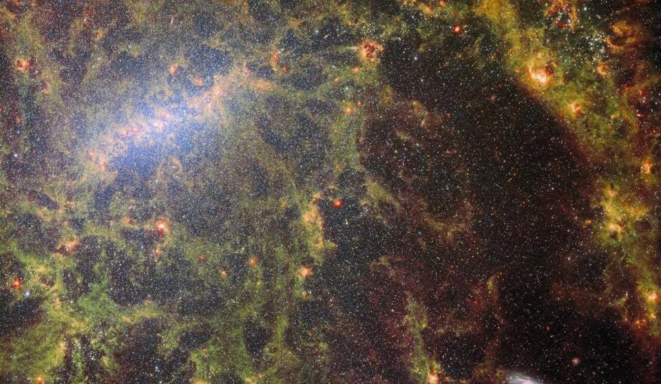 Image of a galaxy showing thousands of stars as tiny white dots against a background of green and yellow ethereal gas.