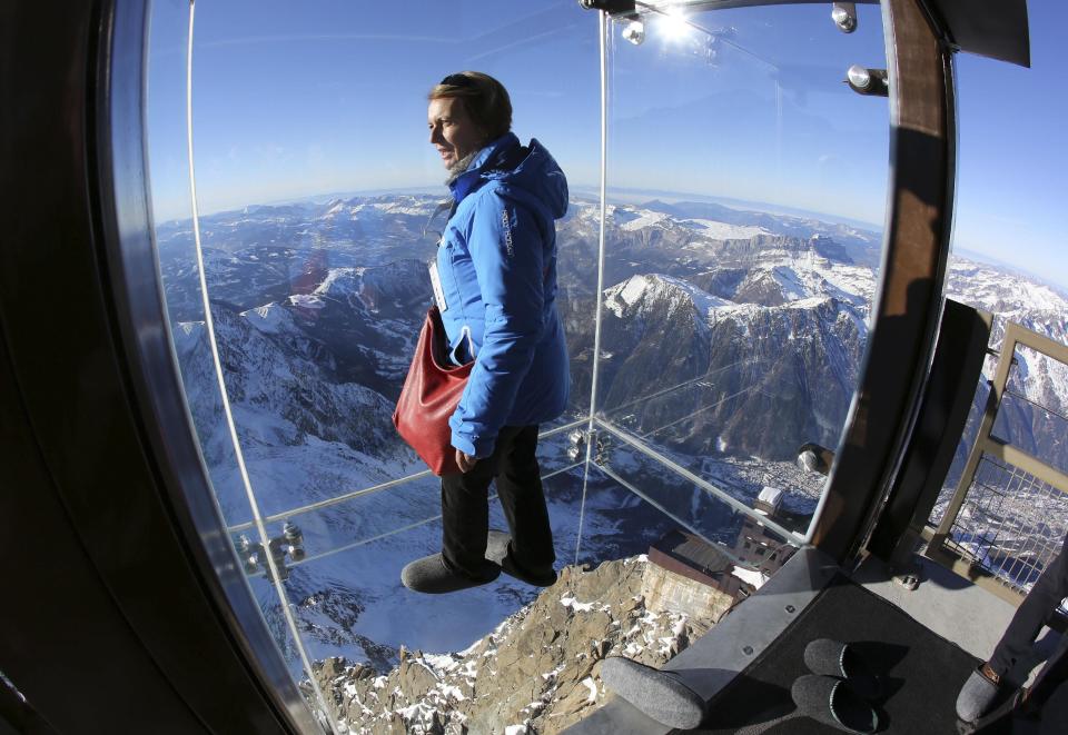 In this photo taken on Tuesday, Dec. 17, 2013, a reporter looks at the mountains through a glass cage named 'Pas dans le Vide' (Step into the Void) at the top of the Aiguille du Midi peak (3842-meters high or 12,604 feet), in the French Alps, during a press visit. Visitors can enjoy the view of Mont Blanc, Europe's highest mountain, from the platform. The attraction opens Saturday. (AP Photo/Alexis Moro)