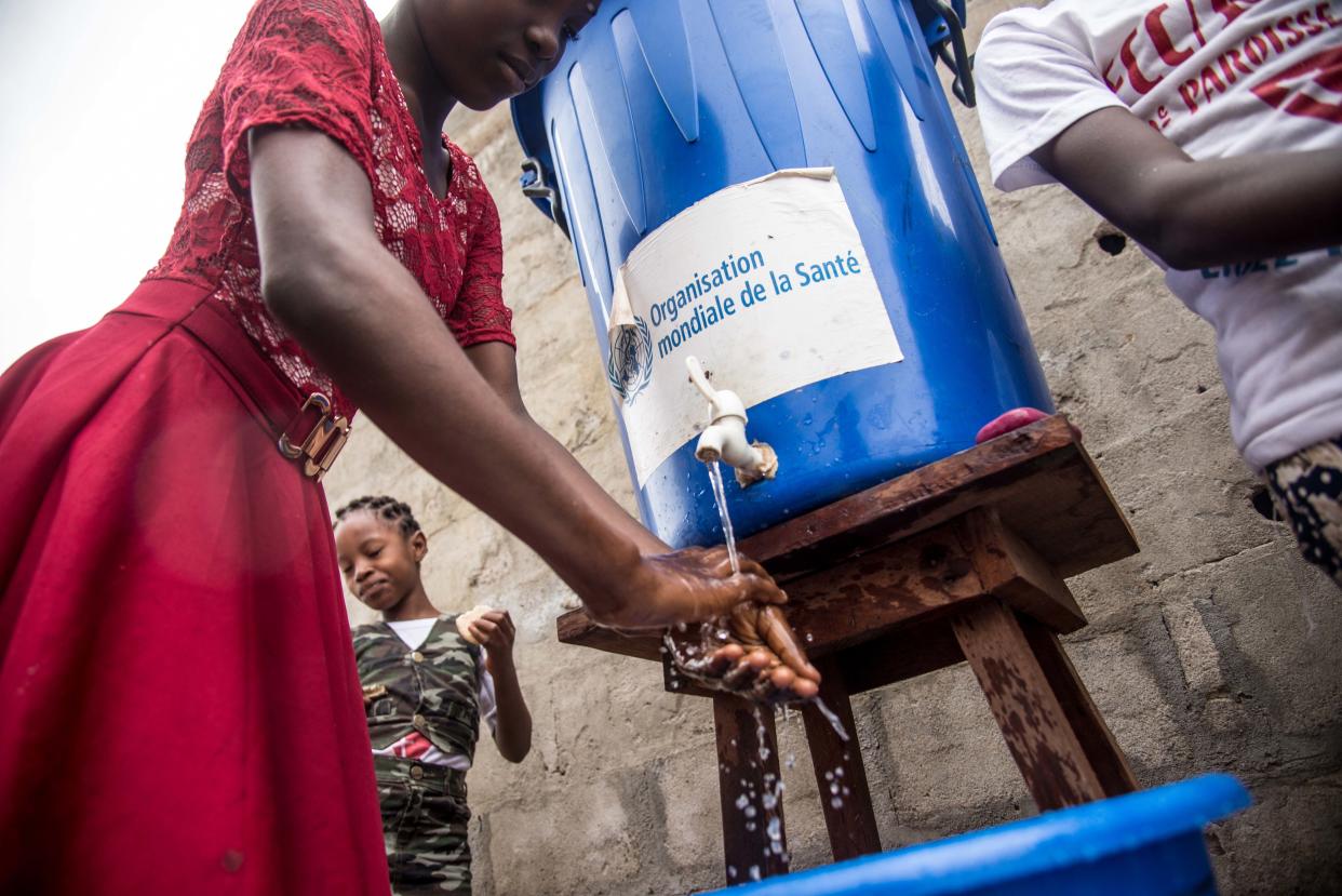 A woman washes her hands from a tank of water bearing a World Health Organization (WHO-OMS) sticker, as a prevention against Ebola virus after a Pentecost mass at the Church of Christ on May 20, 2018 in Mbandaka, northwest of DR Congo. - The Democratic Republic of Congo is preparing to launch an Ebola vaccination programme on May 21 in a bid to stop the latest outbreak of the dreaded fatal disease from spreading, as the UN's World Health Organization (WHO) put the death toll at 25. (Photo by Junior D. KANNAH / AFP) (Photo by JUNIOR D. KANNAH/AFP via Getty Images)