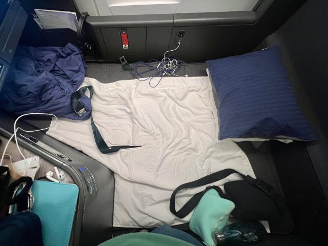 The bed in lie-flat position with the author's purse, pillows, and blanket on top.