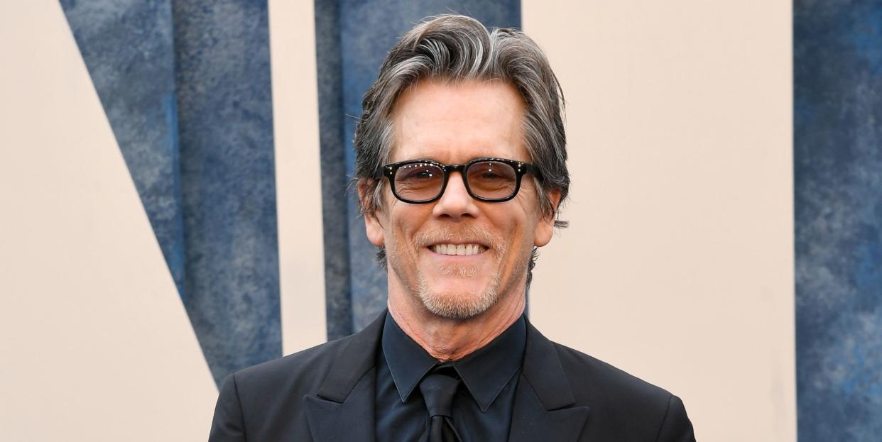 kevin bacon in a black suit and tie with tinted glasses