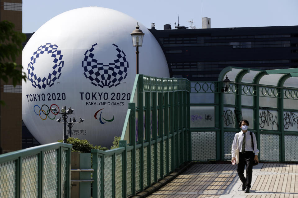 Un individuo con mascarillas camina sobre un puente peatonal, el miércoles 9 de septiembre de 2020, en Tokio, con un despliegue de los Juegos Olímpicos en el fondo. (AP Foto/Kiichiro Sato)