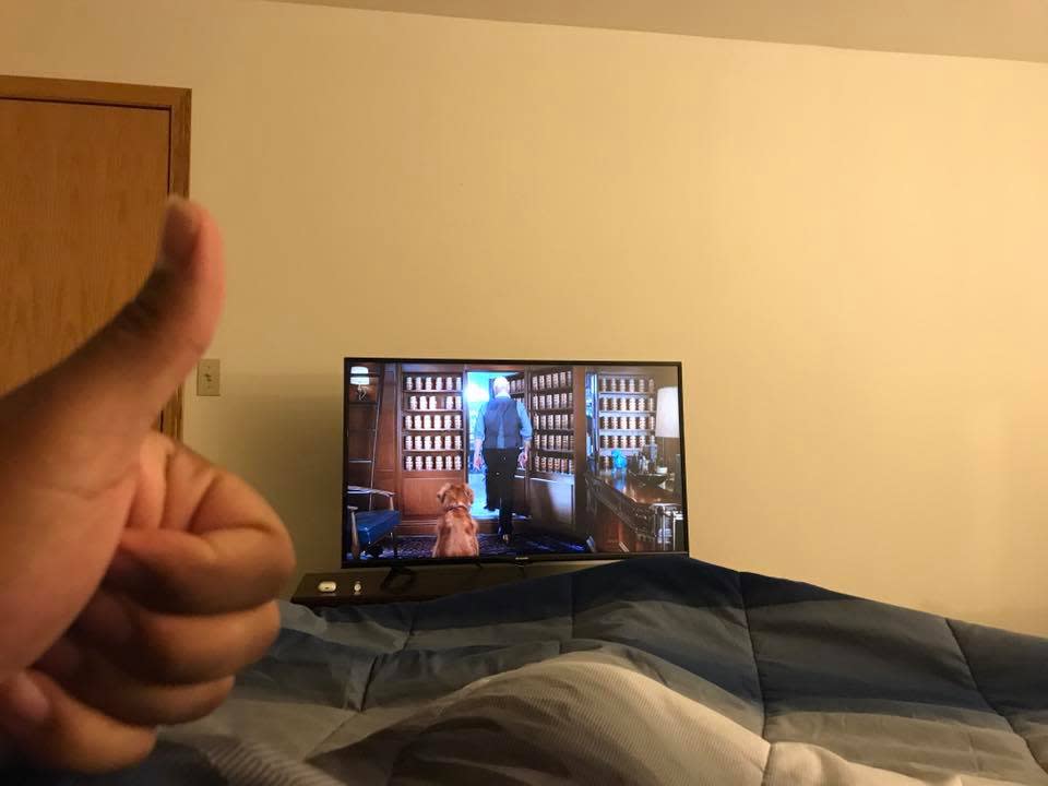 A person's thumb up while sitting in bed watching TV.