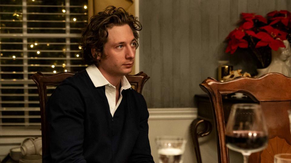 A man with curly hair wearing a black sweater with a white shirt collar and sitting at a dining table in front of poinsettias; still from "The Bear"