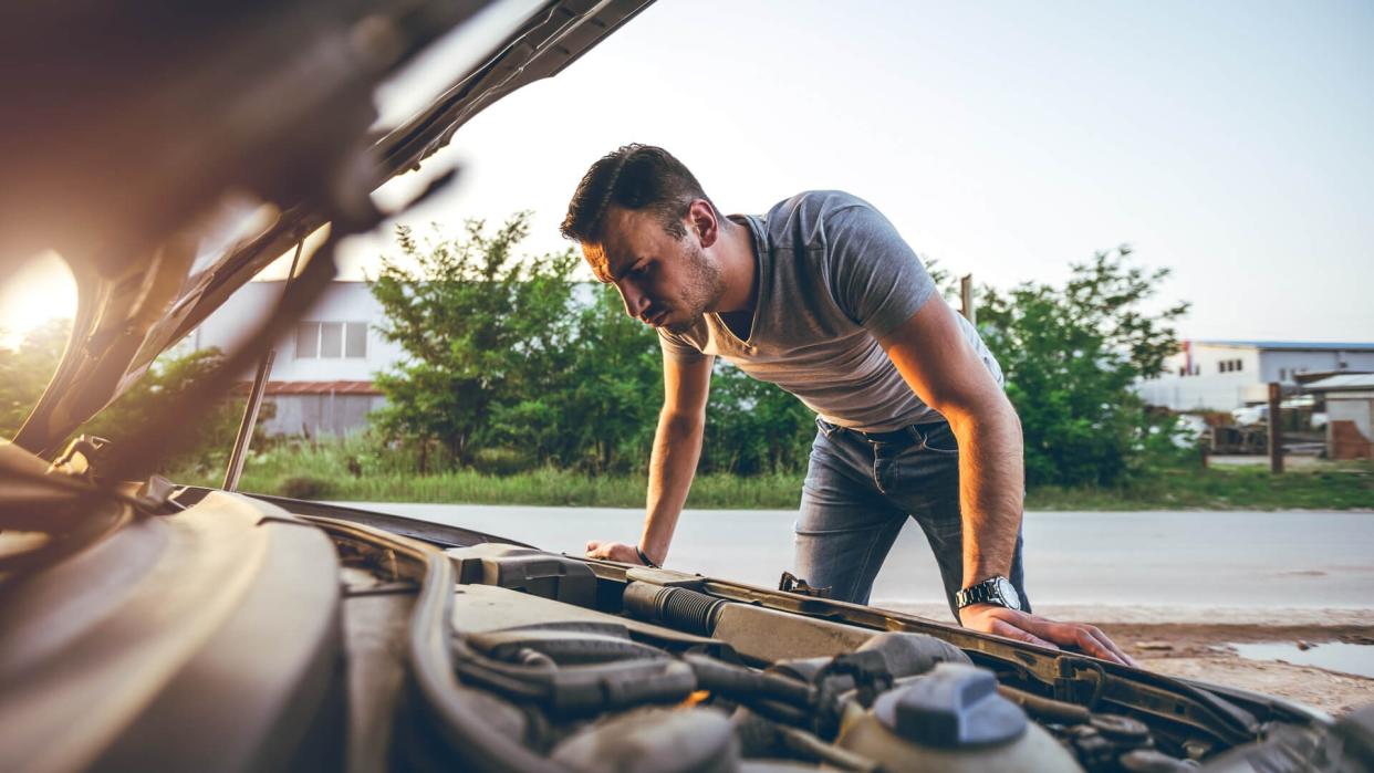 Young man repairing car on the side of the road.