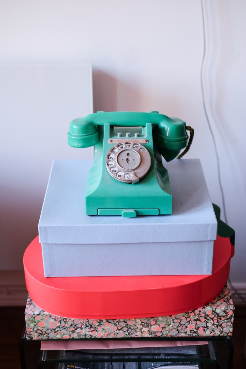 VIntage green phone stacked on colorful boxes in white room.