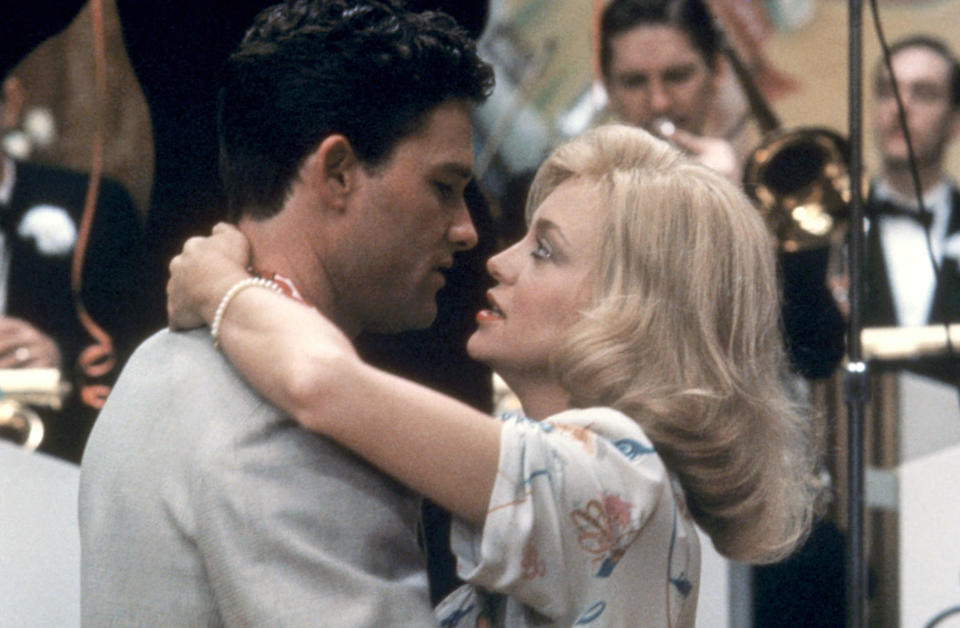 Kurt Russell and Goldie Hawn embrace romantically, with a band performing in the background