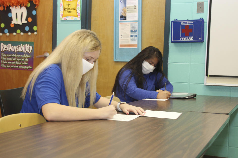 Keeping a seat between them, sophomores' Natalie Brantley, 15, left and Yareny Aguilar-Perez, 15, are introduced to the principles of Early Childhood I at Newton County Career and Technical Center in Decatur, Miss., Monday, Aug. 3, 2020. Thousands of students across the nation are set to resume in-person school Monday for the first time since March. Parents are having to balance the children's need for socialization and instruction that school provides, with the reality that the U.S. death toll from the coronavirus has hit about 155,000 and cases are rising in numerous places. (Janine Vincent/Newton County Schools via AP)