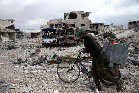 A man walks with his bicycle at a damaged site in the besieged town of Douma, Eastern Ghouta, in Damascus, Syria March 30, 2018. REUTERS/Bassam Khabieh